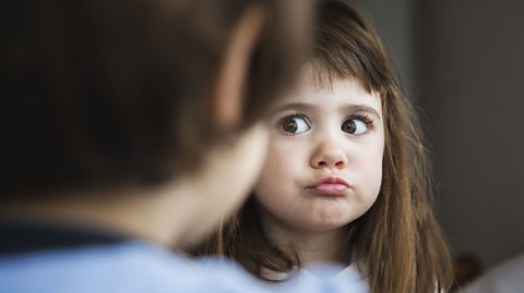 A young girl pulls a face to suggest she's just said something silly or amusing, while looking at a boy with his back to camera