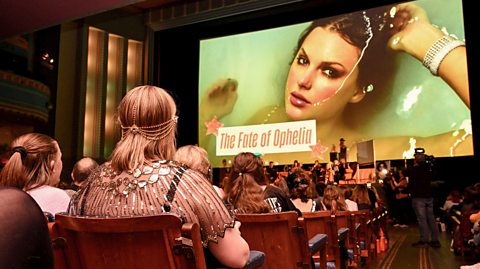 Taylor Swift fans sit in a theatre listening event for her new album The Life of a Showgirl. On screen is a photo of Taylor lying in water, the artwork for her latest album, with the text 'The Fate of Ophelia."