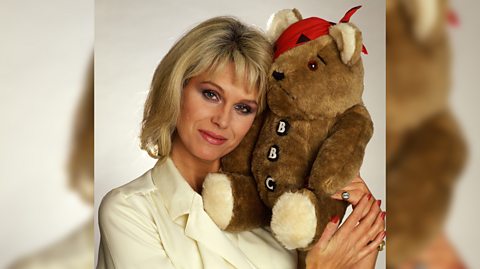 Joanna Lumley posing with the first Pudsey who was brown with a red bandana and buttons
