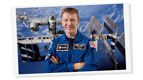 A man smiling into the camera wearing a blue jumpsuit with a Union flag patch on his arm.
