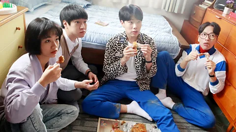 CJ ENM Still of cast members of Reply 1988 sitting on the ground eating chicken wings (Credit: CJ ENM)