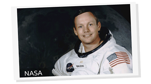A man smiling into the camera wearing a spacesuit with a flag of the USA on his arm.