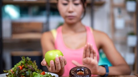 A person holding an apple and a donut