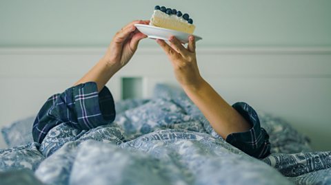 Woman eating a Cheesecake in Pajamas for a Cozy Dessert Moment in bedroom.