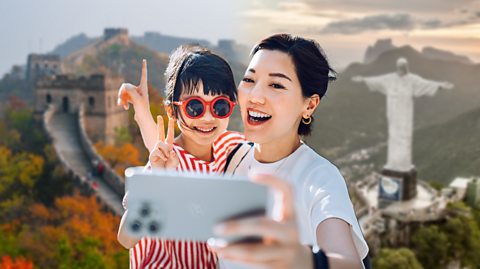 A mum and child smile and take a selfie on their camera phone, pointing to two of the Seven Wonders of the World behind them, the Great Wall of China and Christ the Redeemer
