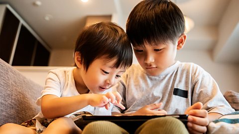 Two young brothers sit together on a sofa using a tablet