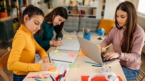 Three sisters study together sat at a table