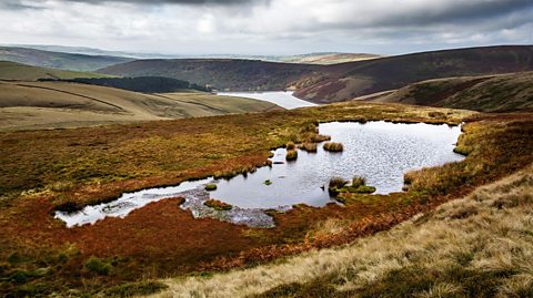 Mermaid's Pool below the summit of Kinder Scout in the Peak District, surrounded by grasses and hills of the plateau. Kinder Reservoir below in the background