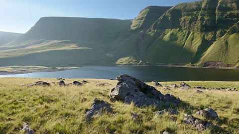 Grassy shore of lake Llyn Y Fan Fach with the towering ridge of the Western Brecon Beacons surrounding it