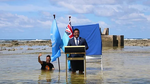 Tuvalu Ministry of Justice, Communication and Foreign Affairs Several years after the Maldives photo, Tuvalu broadcast a speech with a minister at a lectern in the sea (Credit: Tuvalu Ministry of Justice, Communication and Foreign Affairs)