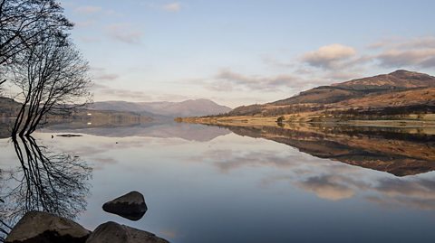 Looking out over Loch Venachar in winter, the Trossach hills, bare trees and clouds reflected in the water