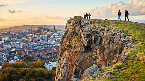 Salisbury Crags, Holyrood Park, with Edinburgh city the in background at sunset. Walkers on the green Salisbury Crags overlook the city beneath them