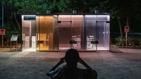 Transparent public toilets in Tokyo designed by Shigeru Ban, featuring smart glass walls that turn opaque when locked with a shadow of a person taking a person in front.