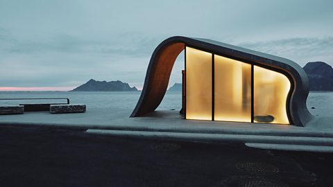 Ureddplassen public toilet in Norway with wave-shaped concrete design and glowing glass walls overlooking Arctic coastline.