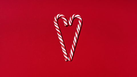 Two candy canes facing each other to form a heart shape. On a deep red background 