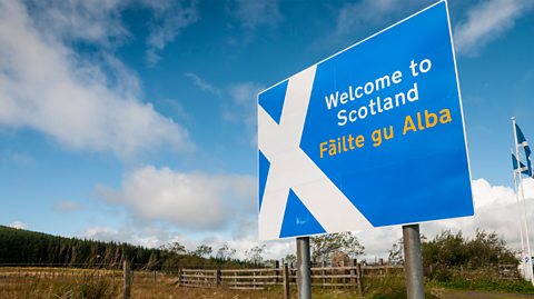 A welcome to Scotland sign at the Scottish border. The sign is blue and white - the country's St Andrew's Cross - and says 'Welcome to Scotland' with the Scots translation of the same phrase beneath it
