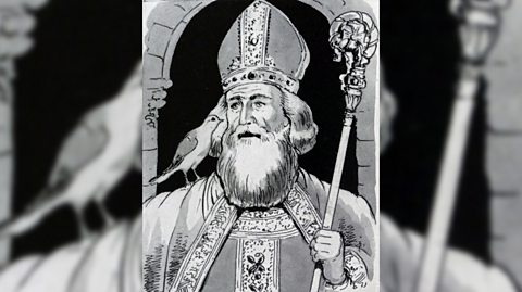 A black and white illustration of St David, patron saint of Wales, wearing religious attire such as robes and a holding a sceptre, with a bird on his shoulder