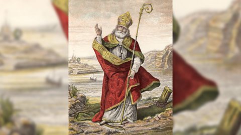 An illustration of St Patrick, patron saint of Northern Ireland, with a sceptre and wearing a red and gold cloak, standing on a snake as he gestures to the sky
