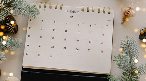 A calendar showing the month of December with Christmas ornaments and tree leaves around it