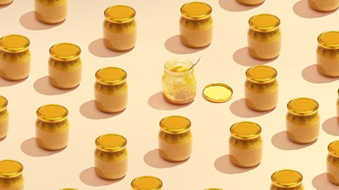 Lots of pots of honey sealed with lids except for one which is open, almost empty and with a spoon in it. 