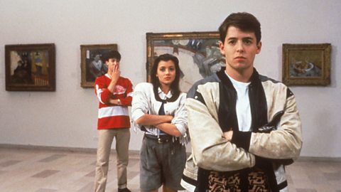 From left to right, Alan Ruck as Cameron Frye in a red hockey jersey, Mia Sara in a white tassled jacket and grey shorts as Sloane Peterson and Matthew Broderick stars as Ferris Bueller,, wearing a beige and black bomber jacket with a leopard print waistcoat. They are in a gallery observing art