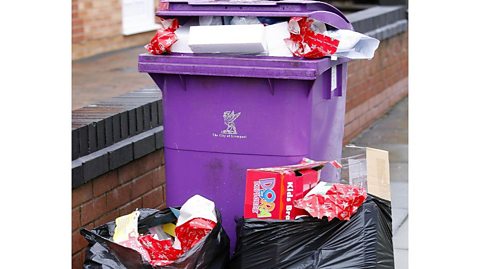 A purple wheelie bin is overflowing with Xmas wrapping and boxes, two black bin bags next to it are also full