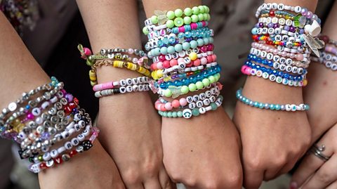 a group of youngsters show off their array of friendship bracelets full of brightly coloured and letter beads, spelling out names