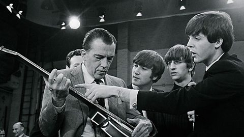 Black and white photo of the Beatles giving US TV host Ed Sullivan a guitar lesson