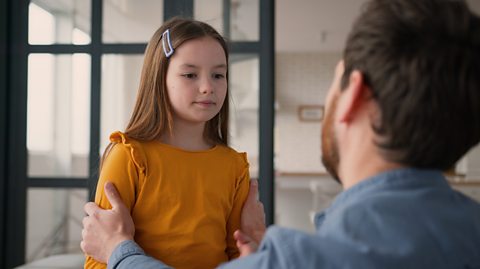 father apologises to daughter, holding her by the arms as she sits on a kitchen work surface while he is level and eye to eye