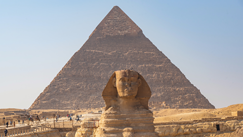 A photo of the Sphinx in front of the pyramids.