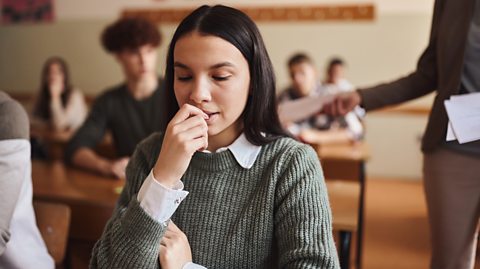 young teen woman chews nails nervously as she await exam in school hall