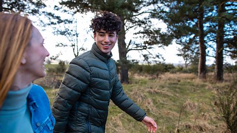 Teenage boy and his red headed mum walking in cold weather through pine woods and grassland smiling as they chat