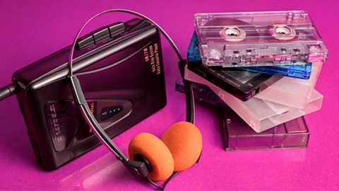 An 80s cassette player, piles of tapes and cases and headphones with orange pads over them against a pink background