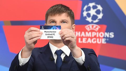 Andrey Arshavin holds a card reading 'Manchester United FC (ENG)' as part of the Uefa Champions League draw. The tournament logo is on a wall behind him