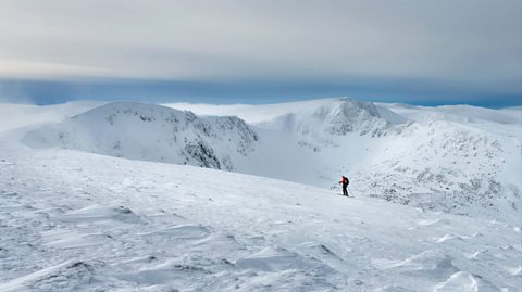 Snowy scenes in Cairngorms, Scotland. The national park is covered in snow and one hiker can be seen walking through the mountains in the distance