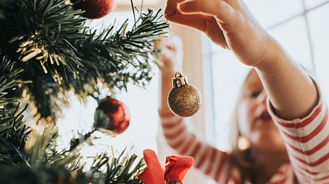 Close-up of a person hanging a gold Christmas ornament on a decorated tree with red baubles and ribbon