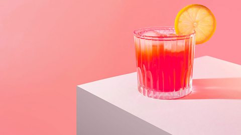 Short cocktail glass with red drink, ice and a slice of lemon on the side 