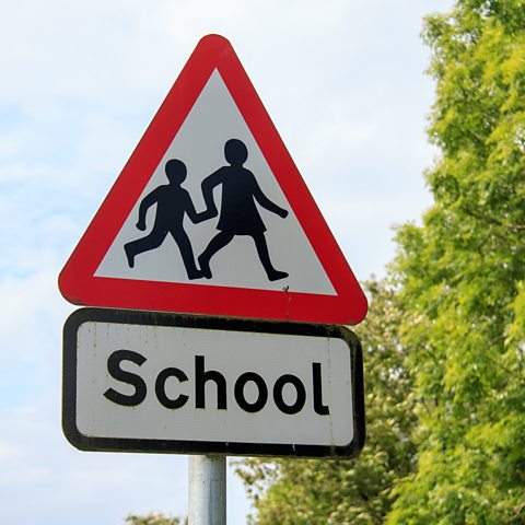A typical British School sign - a triangle with a red border and a girl and boy walking hand in hand above a sign saying 'school'