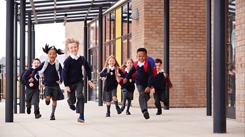 a group of UK primary school children in uniform run towards the camera as they leave their school for holidays.
