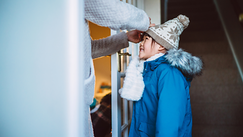 A parent puts a wooly hat on their child.