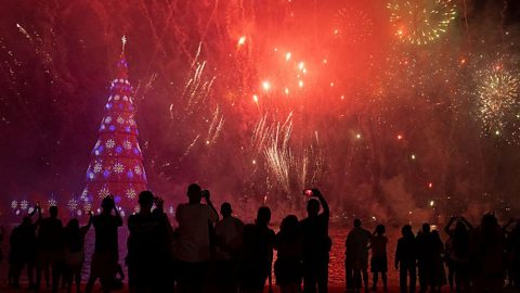 Floating Christmas tree illuminated with blue and purple lights during a fireworks display over water in Rio de Janeiro, Brazil.