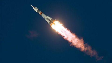 Soyuz TMA-19M spacecraft is seen in the sky shortly after launch, rockets blasting bright white, yellow and orange flames