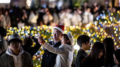 Getty Images Couple taking a selfie in a crowd with Christmas lights behind in Tokyo (Credit: Getty Images)