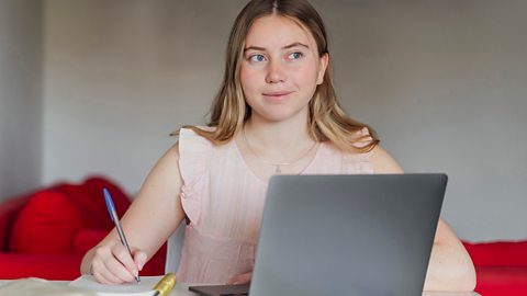 Secondary school student at home with notepad and laptop, taking quizzes for exam prep