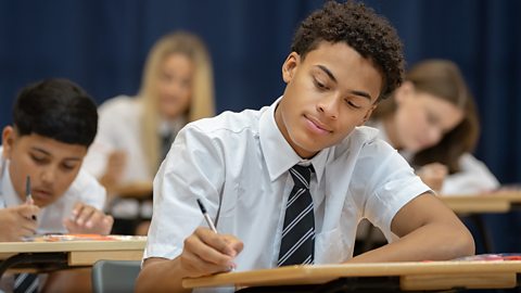 GCSE schoolboy sitting an exam in a school hall with pen and paper, other students in background