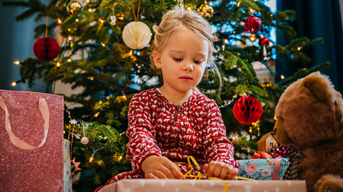 A child opens a bow on the top of her Christmas present.