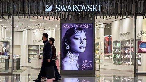 An electronic advertisement board with Ariana Grande and Swarovski on it.