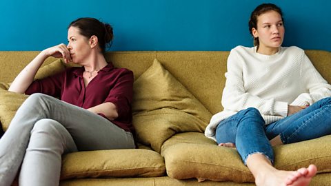 Mother and teenage daughter having an argument look away from each other on a sofa