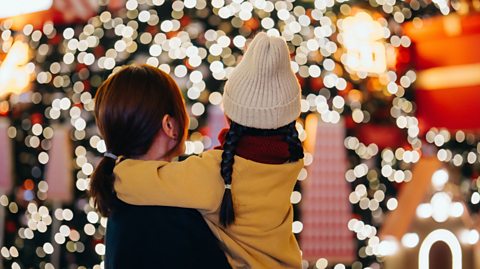 Rear view of mother carrying her daughter in her arms, looking at an illuminated Christmas tree in a Christmas market