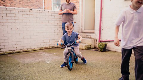 Child on bike in yard with dad and brother